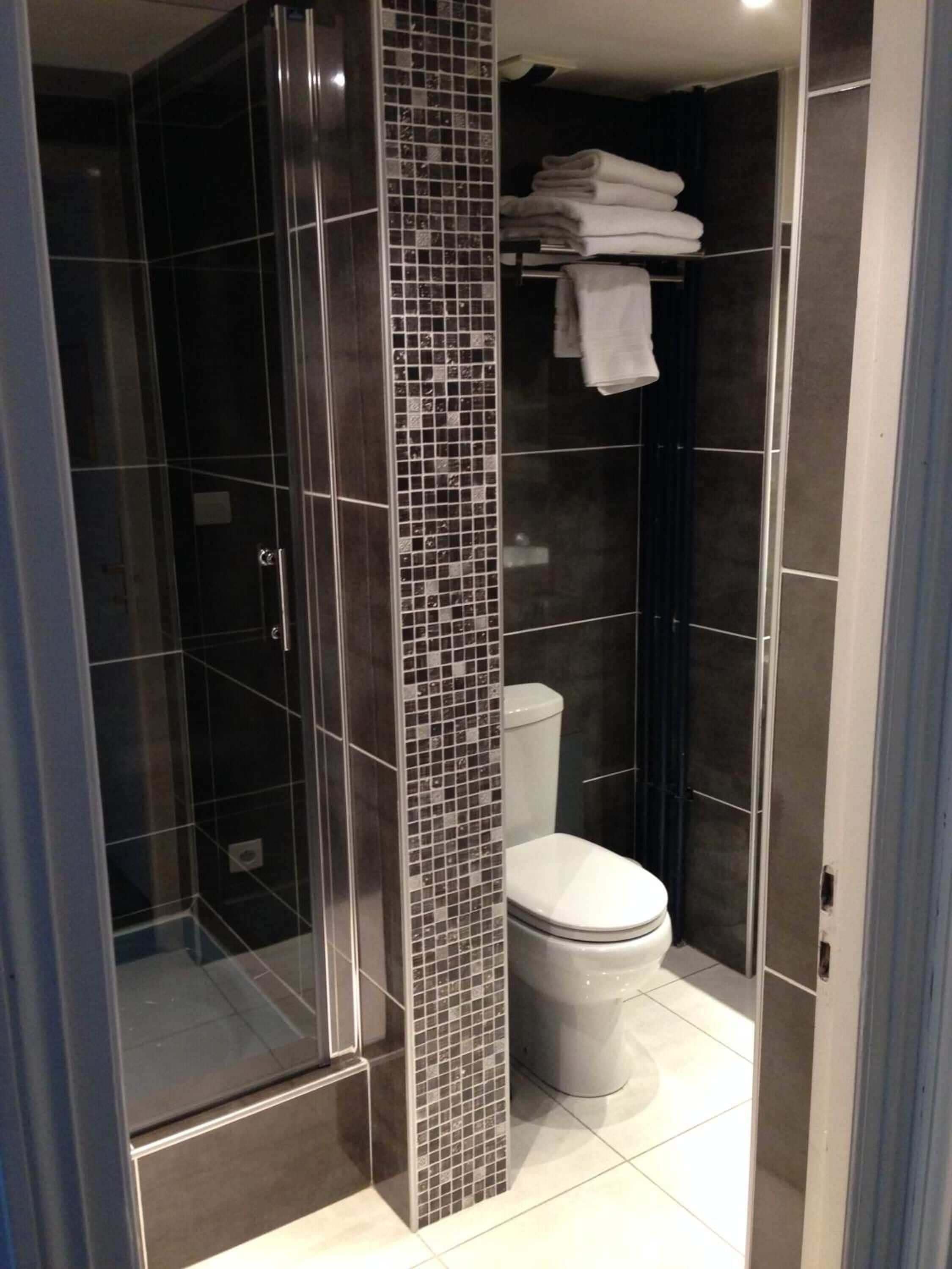 A modern bathroom with a glass-enclosed shower, a tiled wall, and a toilet.