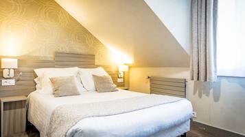 A hotel room with a large bed, two bedside lamps, a wooden headboard, and a window with curtains.