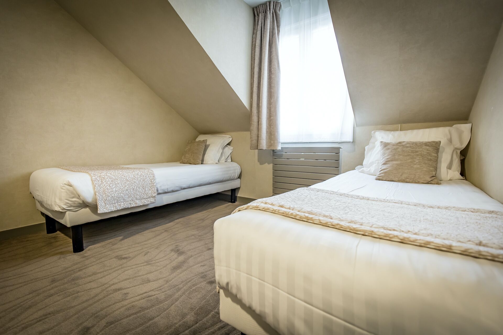 A bedroom with two beds, a window with curtains, and a sloped ceiling.