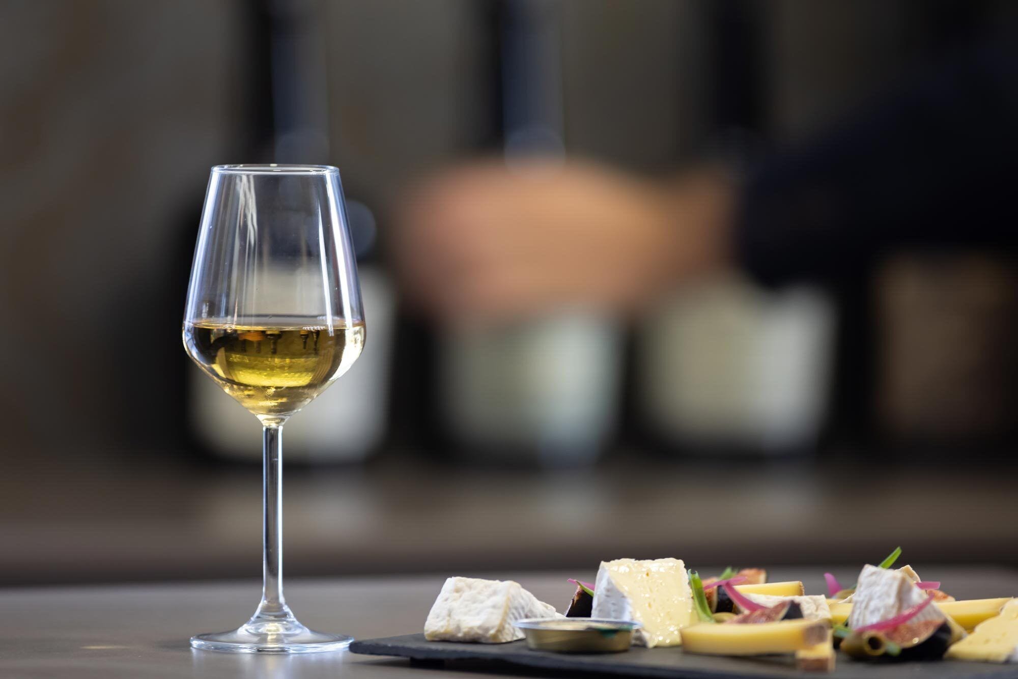 Ein Glas Weißwein auf einem Tisch mit verschiedenen Käsesorten und Crackern.