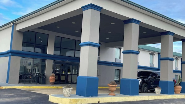 Un hotel con vestíbulo cubierto, amplias ventanas y un estacionamiento con un coche negro.