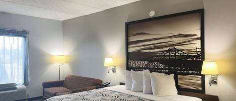 A hotel room with a large bed, two bedside lamps, a chair, a window with curtains, and a wall-mounted artwork.