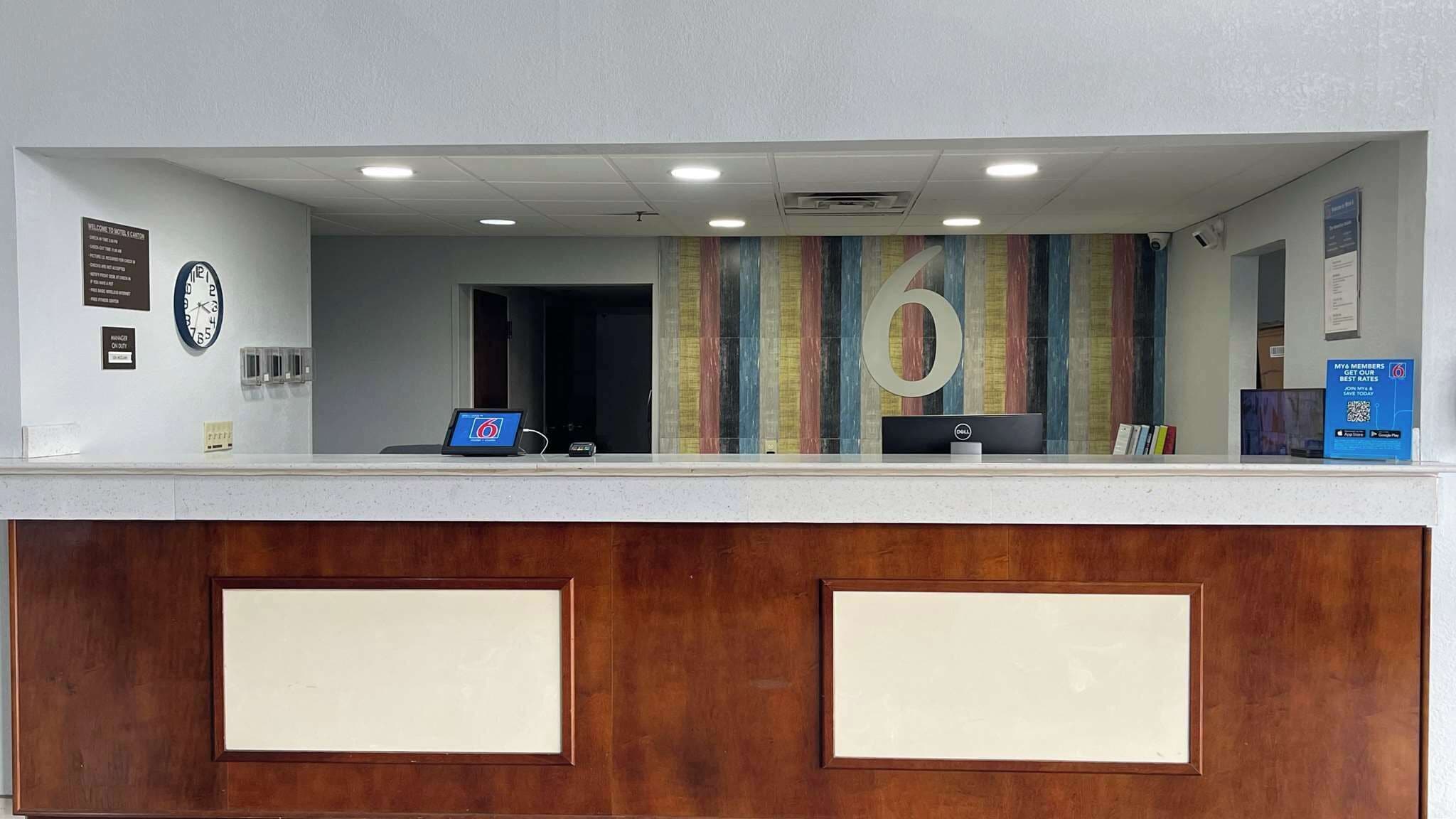 A hotel reception desk with a clock, a digital display, and a large 'O' decoration on the wall.