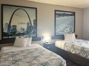 A hotel room with two beds, each with patterned bedding. There are two framed pictures on the wall, one depicting a cityscape and the other a road sign. - Motel 6 Canton, MS (Canton)
