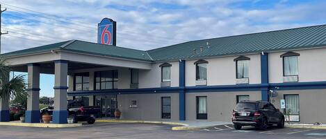 A motel with a covered parking area, multiple rooms, and a prominent '6' sign on the building.