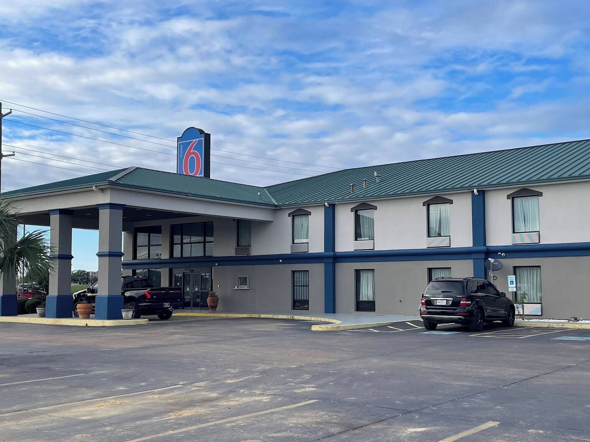 Un motel con zona de estacionamiento techada, varias habitaciones y un llamativo letrero con el número 6 en el edificio.