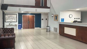 Eine großzügige Lobby mit einer Rezeption, einer großen Holztür, einem Mülleimer und einem gerahmten Bild an der Wand.