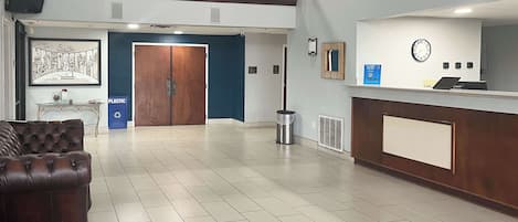 A spacious lobby with a reception desk, a large wooden door, a trash can, and a framed picture on the wall.