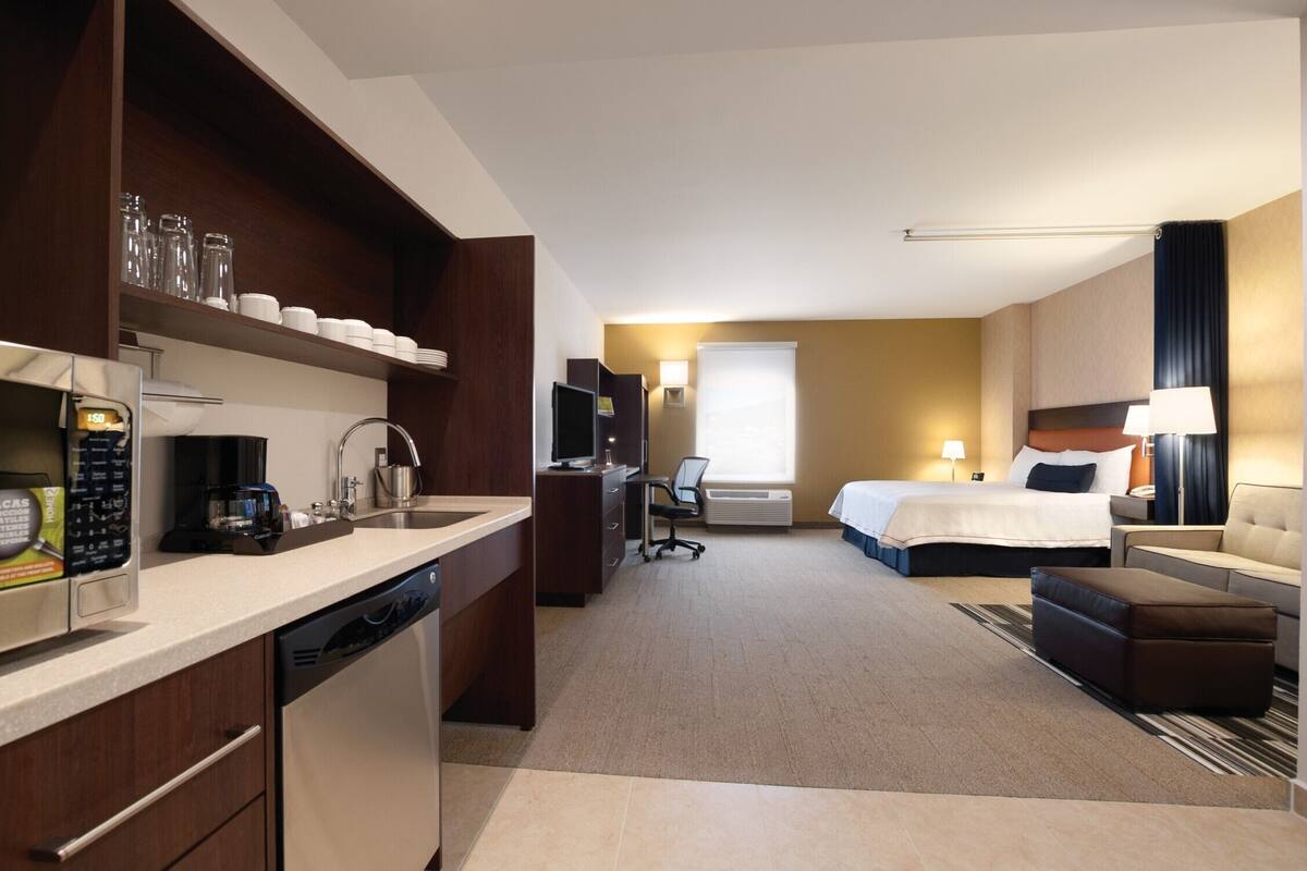 A hotel room with a kitchenette, a bed, a desk, and a TV.