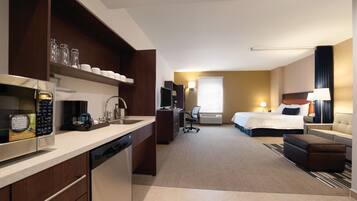 A hotel room with a kitchenette, a bed, a desk, and a TV.