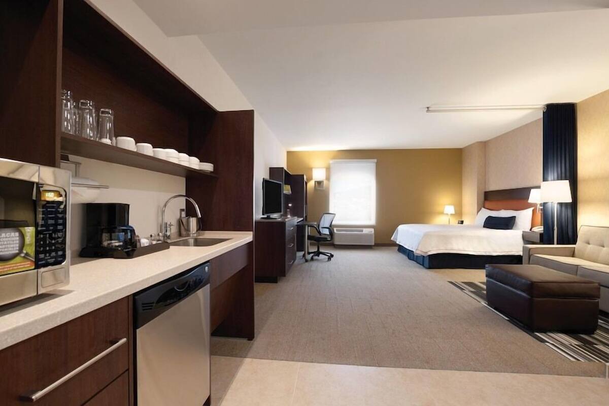 A hotel room with a kitchenette, a bed, a sofa, a desk, and a TV.