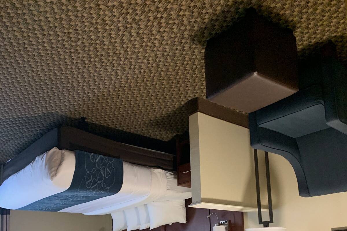 Une chambre d’hôtel compacte comprenant un lit superposé, une table de chevet avec une lampe, une petite table de chevet et une étagère fixée au mur.