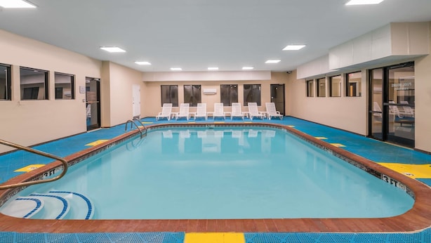 A swimming pool with clear blue water, surrounded by white lounge chairs and a wooden deck. - Comfort Suites Cordova (Cordova)