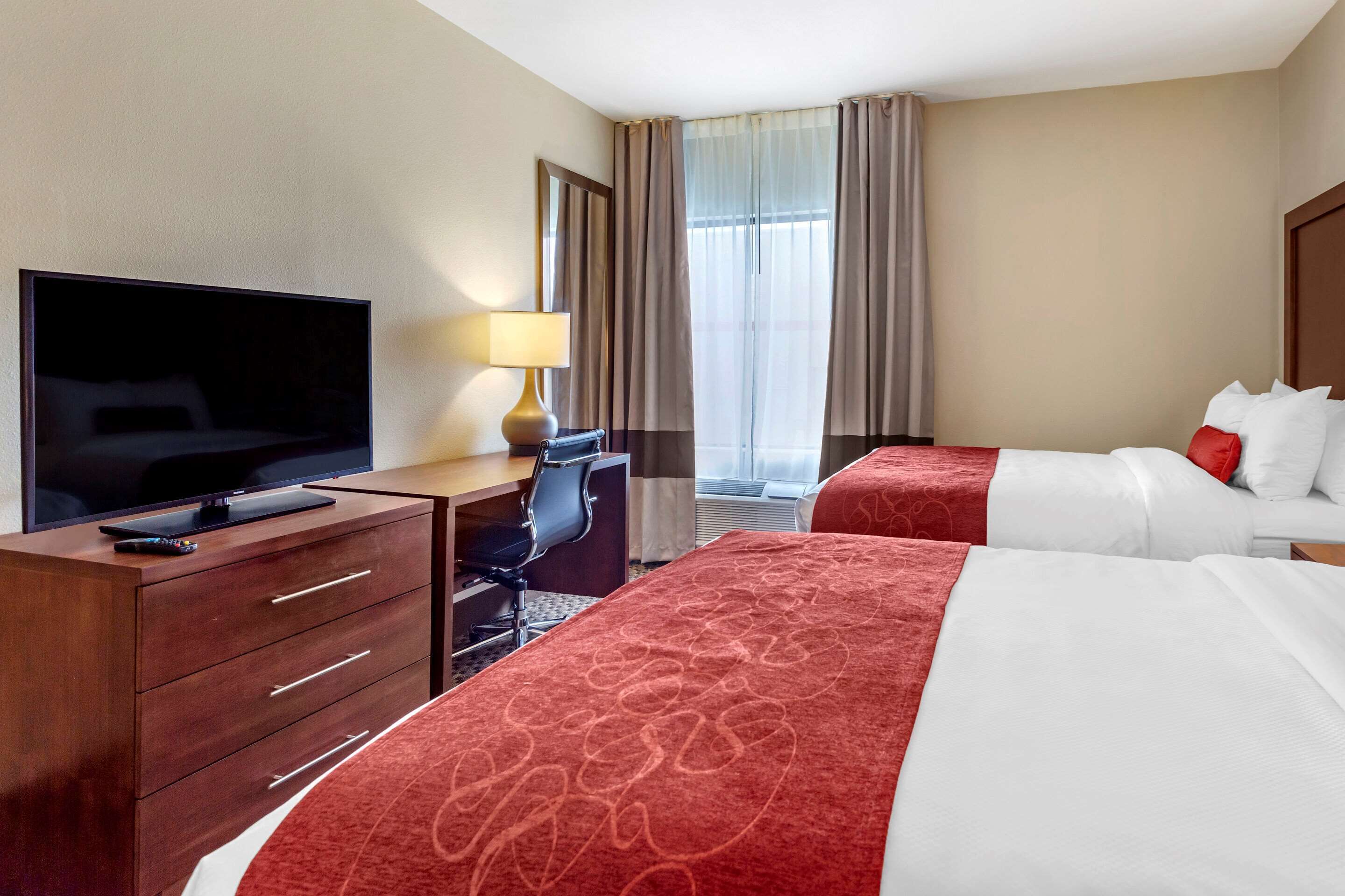 Une chambre d’hôtel équipée d’une télévision, d’un bureau, de deux lits et d’une fenêtre avec des rideaux.