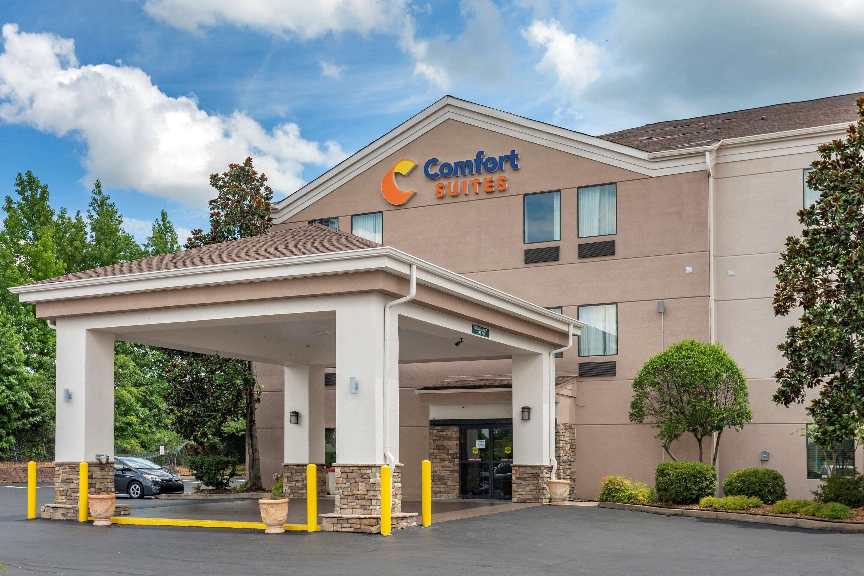 A Comfort Suites hotel with a covered entrance, a parking lot, and a clear sky.