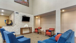 A hotel lobby with blue sofas, a stone accent wall, a flat-screen TV, and a small table with decorative items. - Comfort Suites Cordova (Cordova)
