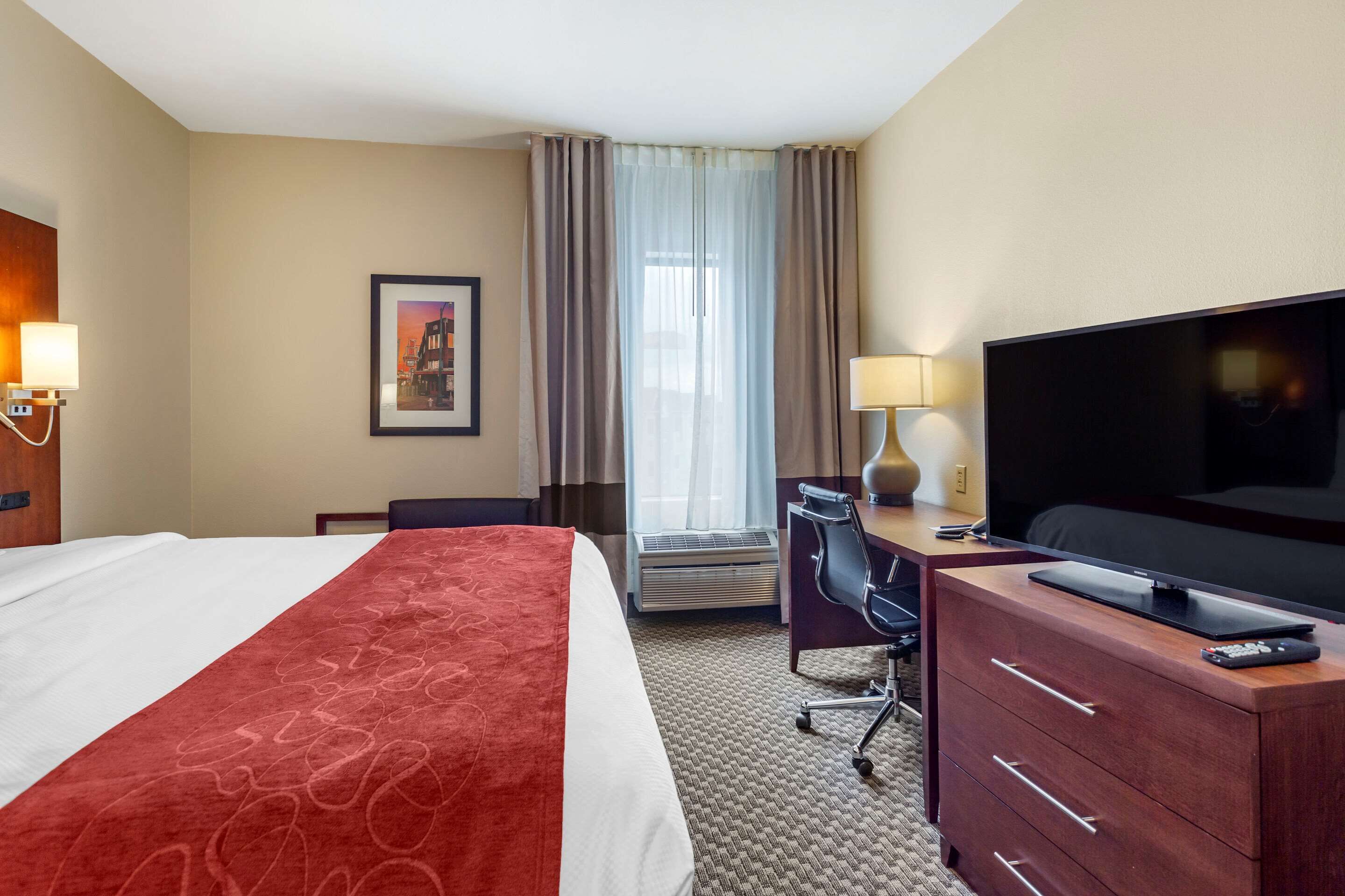 A hotel room with a bed, a desk, a television, and a window with curtains.
