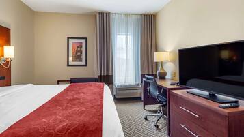 A hotel room with a bed, a desk, a television, and a window with curtains.
