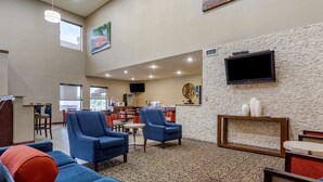 A spacious lobby with blue armchairs, a patterned carpet, a television mounted on a textured wall, and a view of the outside through large windows. - Comfort Suites Cordova (Cordova)