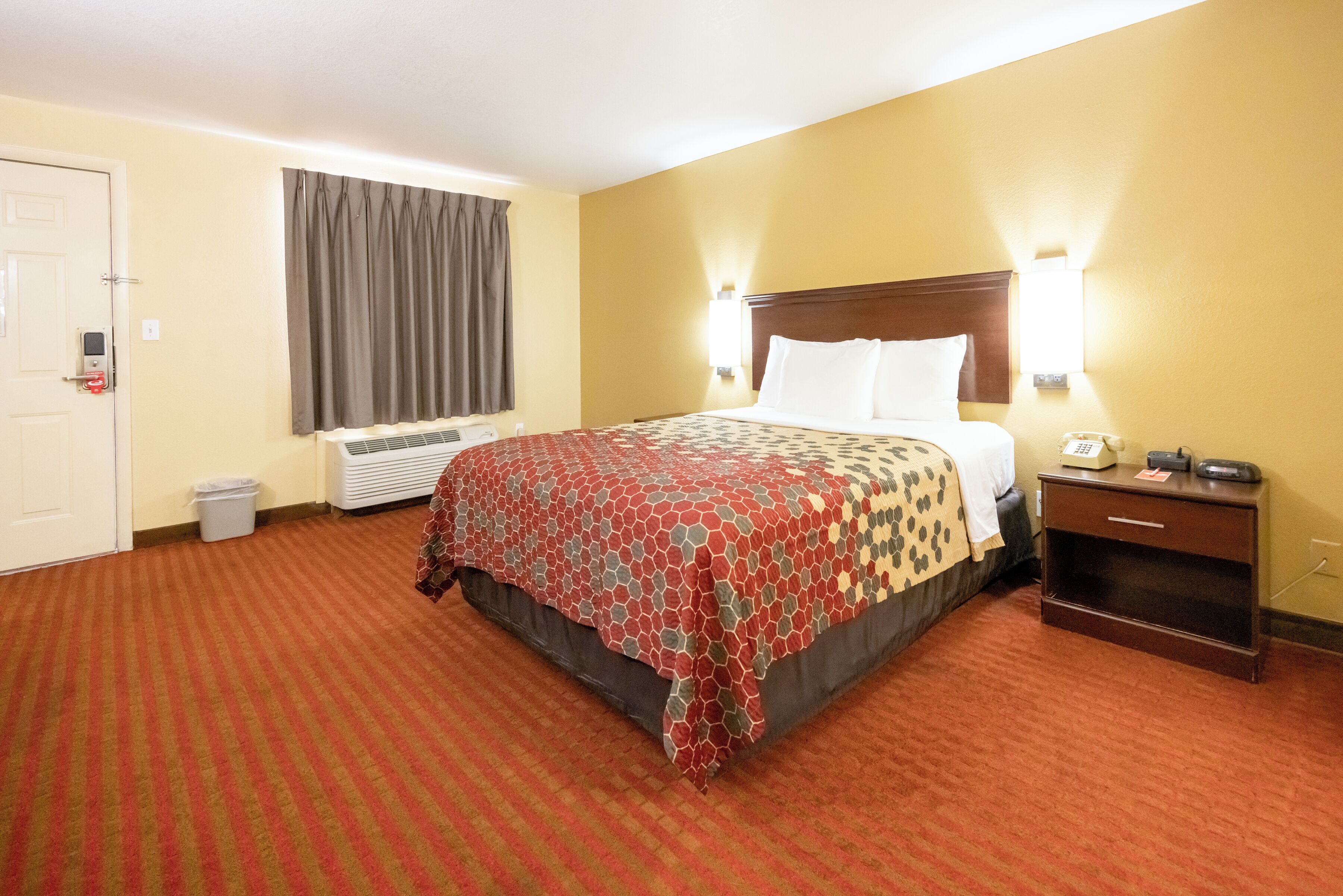 A hotel room with a large bed, a nightstand, a telephone, and a wall-mounted light fixture.