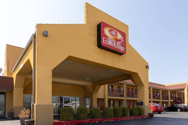 A hotel with a yellow facade, a red sign reading "EconoLodge," and a parking lot with several cars. - Econo Lodge McAlester (McAlester)