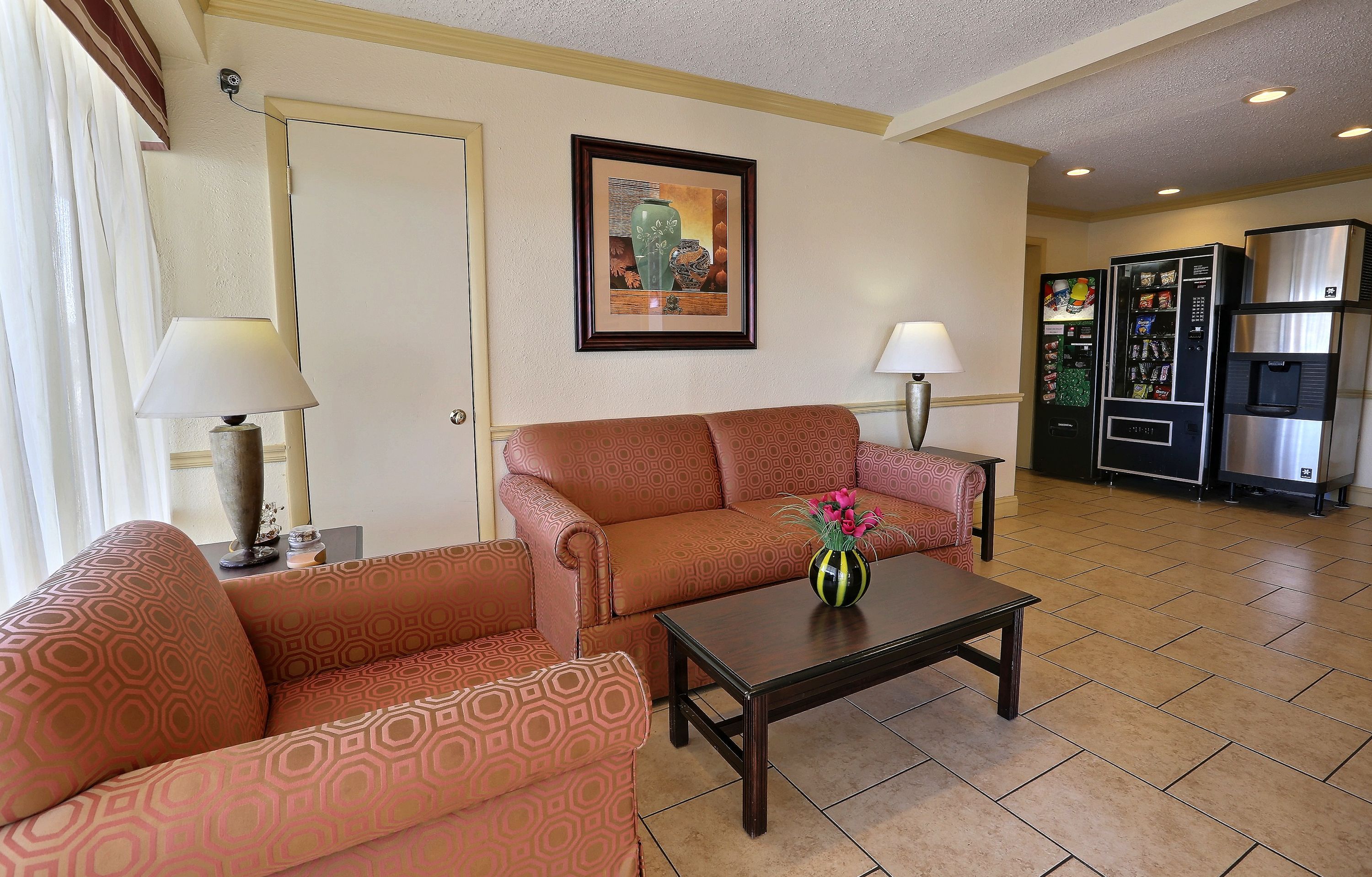 A hotel room with a sofa, a coffee table, a framed picture on the wall, a door, and a refrigerator.