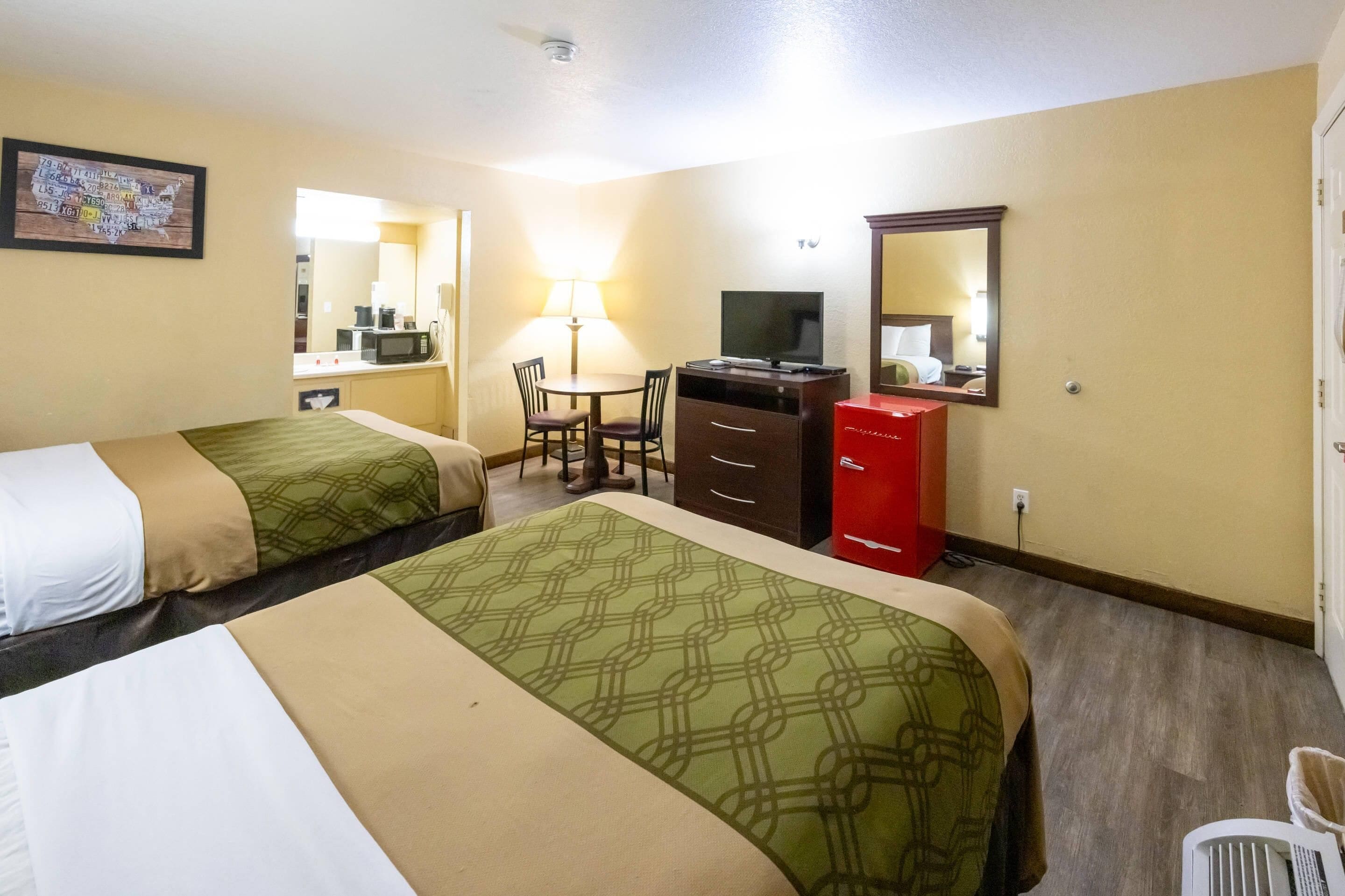 Habitación de hotel con dos camas, un escritorio con silla, televisor, un armario rojo y un espejo en la pared.