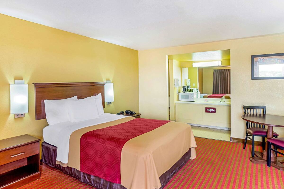 Quarto de hotel com cama, mesa de cabeceira, abajur e pequena escrivaninha com cadeira.