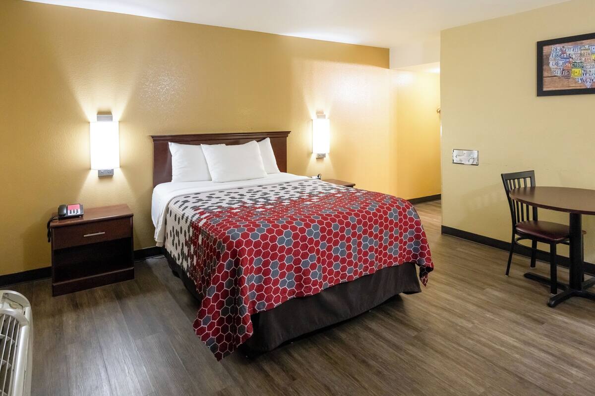 Quarto de hotel com uma cama, mesas de cabeceira, escrivaninha e uma cadeira.