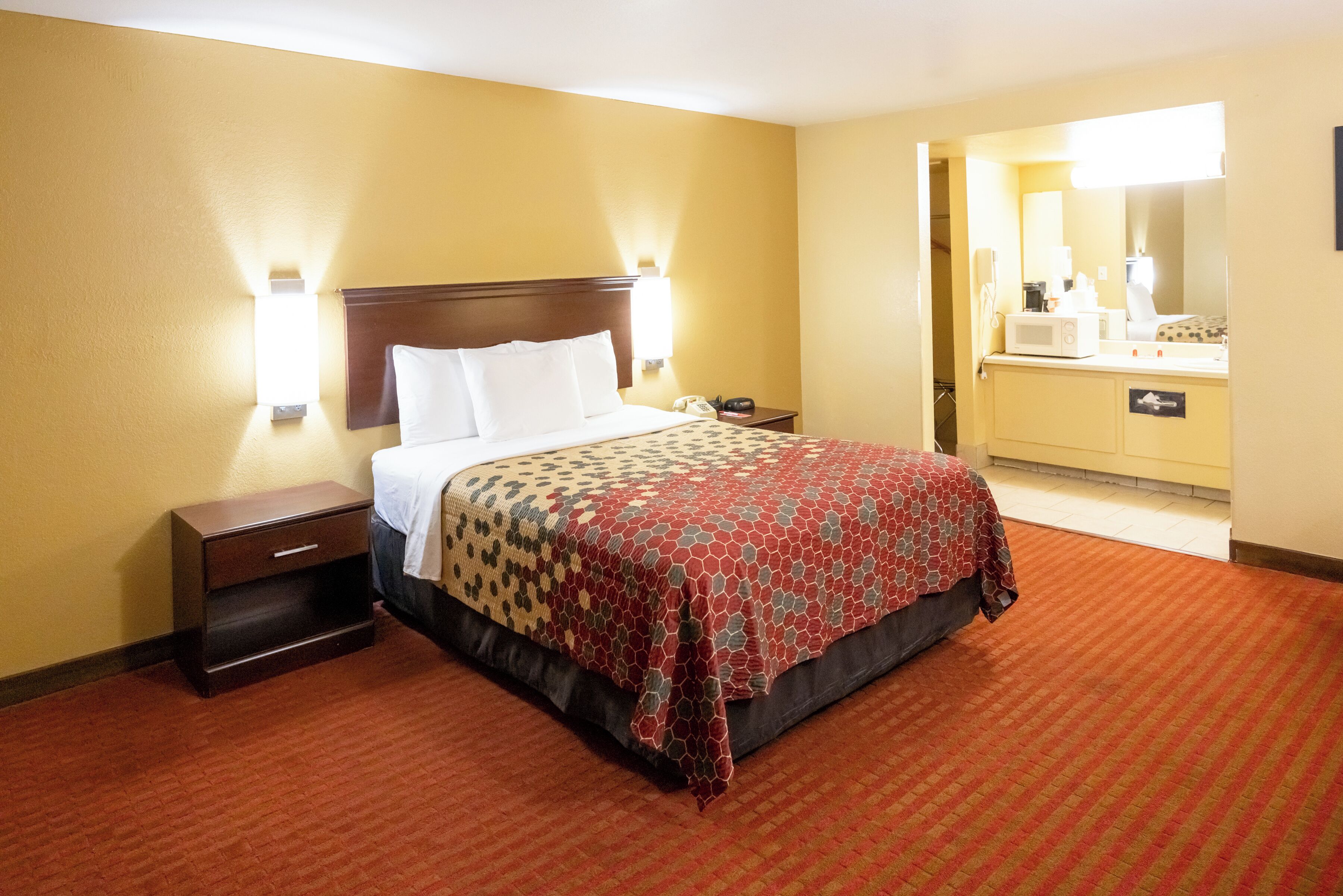 Una habitación de hotel con cama, mesita de noche, lámpara y espejo de baño.
