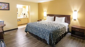 Una camera d'albergo con un letto grande, un comodino, una scrivania con una sedia e un bagno visibile attraverso una porta aperta.