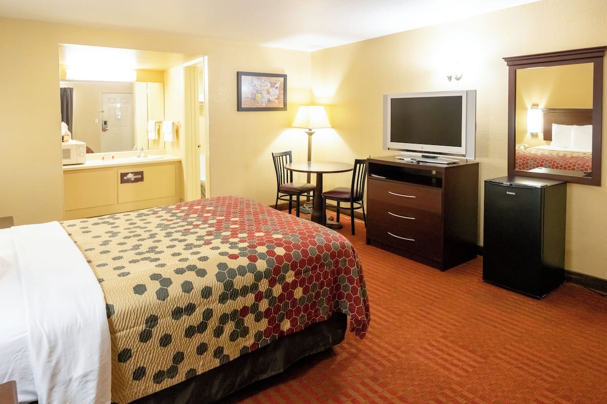 Quarto de hotel com cama, escrivaninha, televisão, luminária e refrigerador.