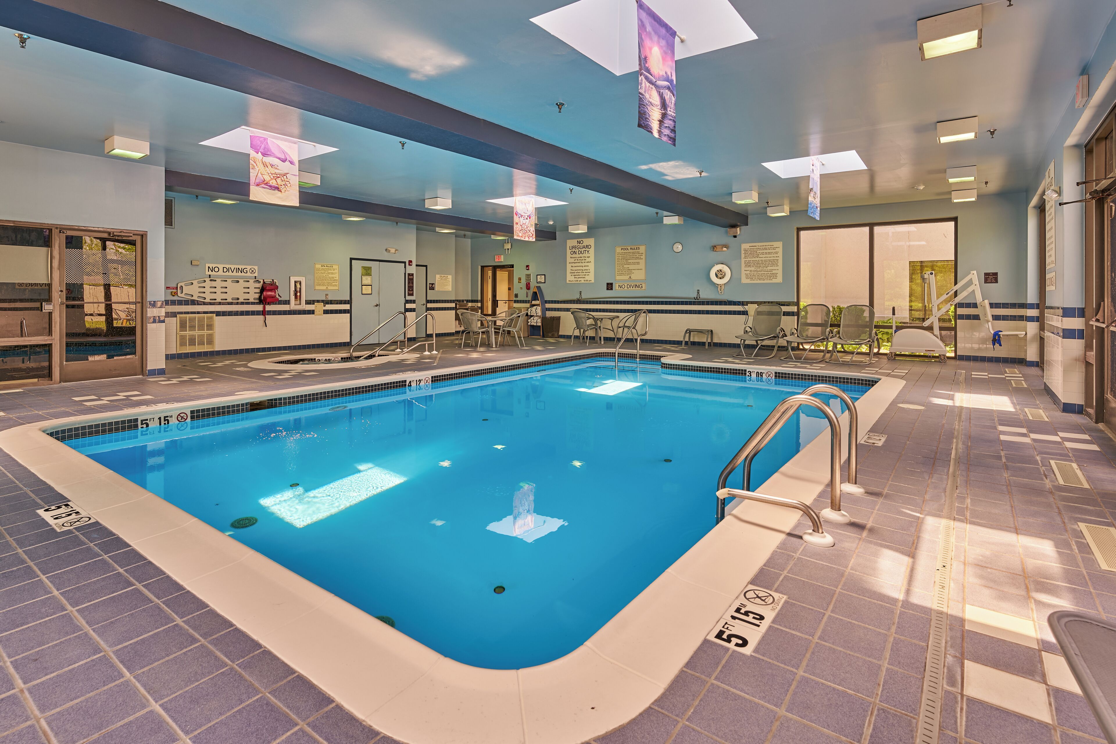 A large indoor swimming pool with clear lane markings, a lifeguard chair, and a no diving sign.