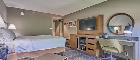 Una habitación de hotel con cama, escritorio, silla, televisor y espejo.