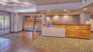 Vestíbulo de hotel con una recepción, un letrero de bienvenida, un rincón para snacks infantiles y vistas al exterior.