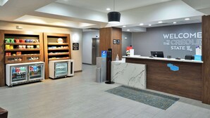 Zona de recepción de un hotel con un mostrador de mármol, máquinas expendedoras y un cartel de bienvenida.