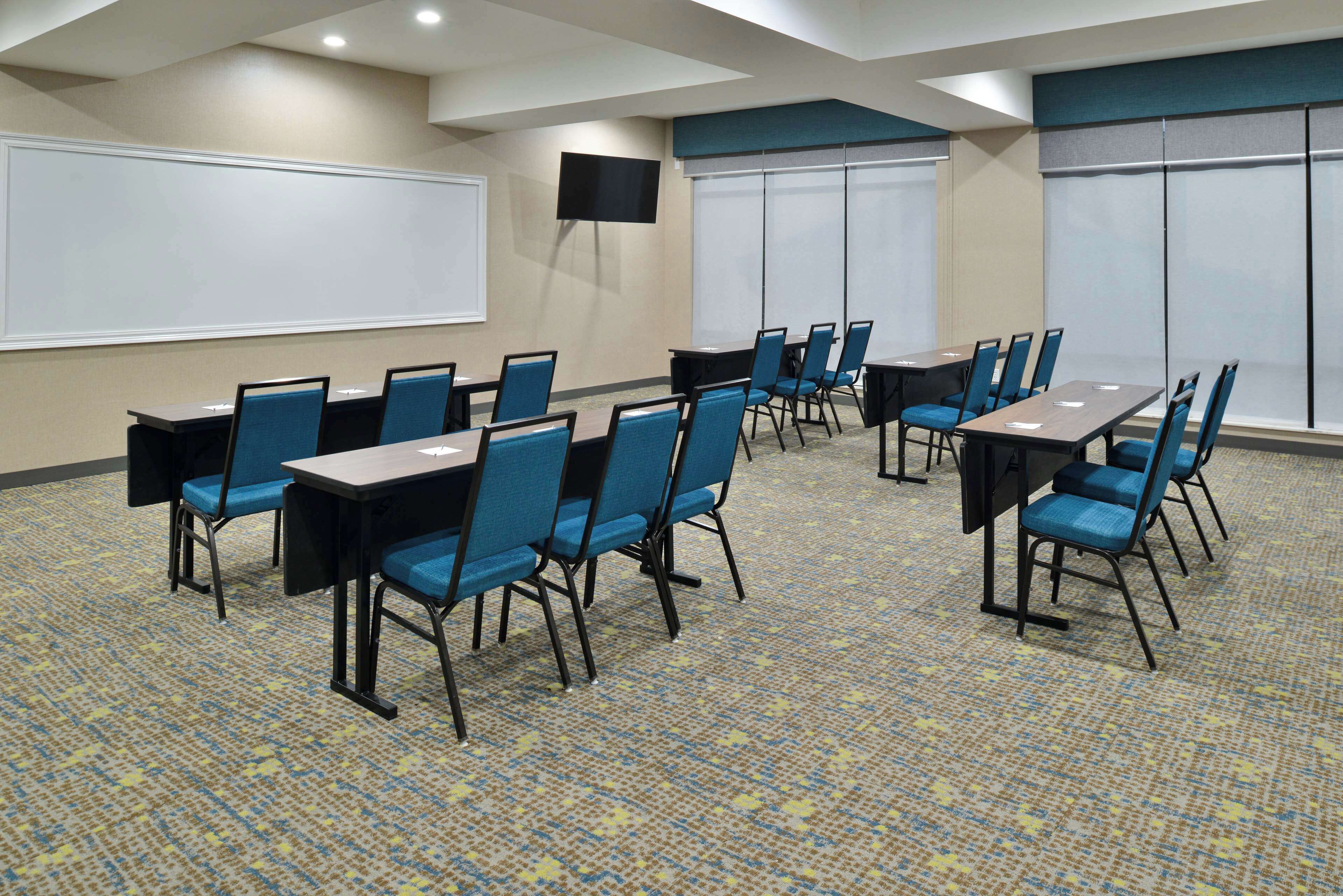 A conference room with multiple tables and chairs, a whiteboard, and a TV screen.
