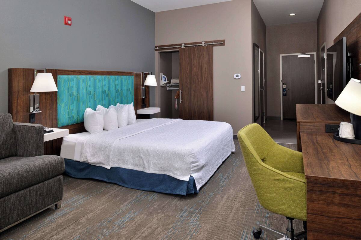 Hotelkamer met een bed, een bureau, een stoel, een nachtkastje, een lamp, een kledingkast en een deur naar de badkamer.