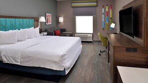 Habitación de hotel con una cama grande, un escritorio, una silla, un televisor y una ventana con persianas.