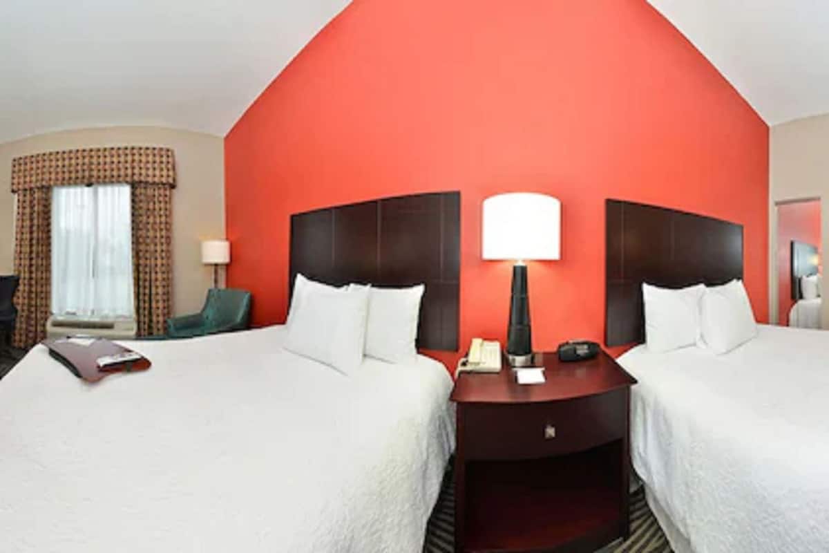 Een hotelkamer met twee bedden, een bureau, een lamp en een raam met gordijnen.