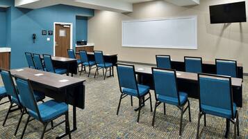 A conference room with multiple tables and chairs, a whiteboard, and a flat-screen TV on the wall.