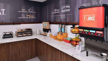 Una encimera de cocina con un dispensador de zumo, una cafetera y diversos utensilios de cocina.