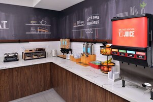 Una encimera de cocina con un dispensador de zumo, una cafetera y diversos utensilios de cocina.