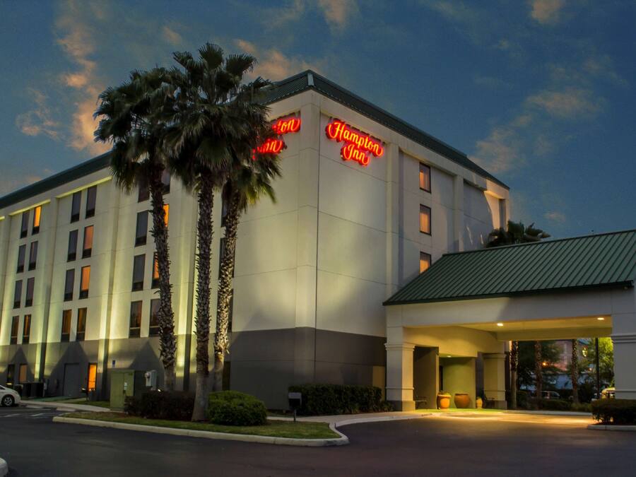 Un hotel de diseño moderno, con una entrada destacada que cuenta con un área cubierta y un cartel que dice "Hampton Inn".