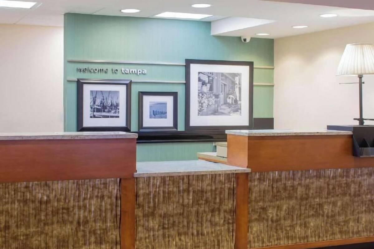 A reception desk with framed pictures on the wall, a 'Welcome to Tampa' sign, and a lamp on the right.