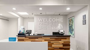 Un comptoir d’accueil au design en bois, une pancarte indiquant « Bienvenue au pays du soleil et de la lumière », et une autre pancarte « Hilton Honors ».