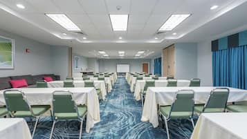 Una sala conferenze con file di tavoli e sedie, pavimento rivestito di moquette e uno schermo per proiettore.
