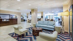 A hotel lobby with a reception desk, a blue sofa, two armchairs, a patterned rug, and a decorative tree trunk. - Hampton Inn Wilmington-Medical Park (Wilmington)