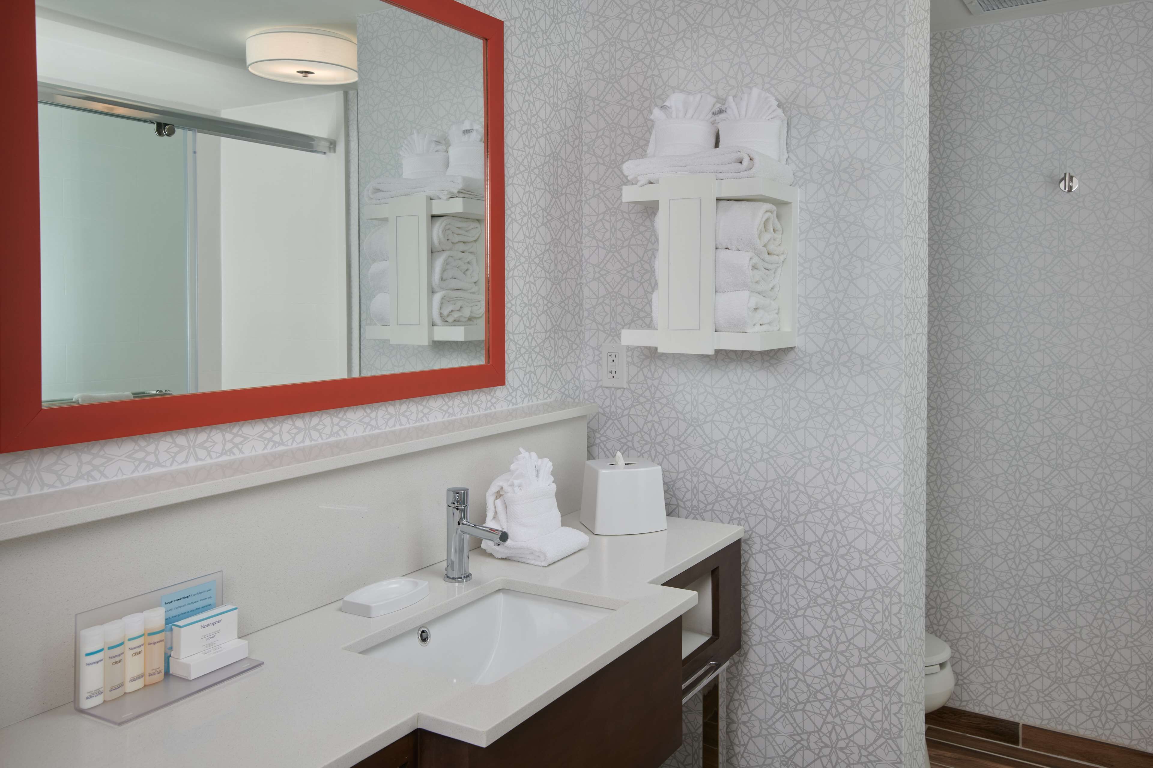 A modern bathroom with a large mirror, white sink, and towel racks.