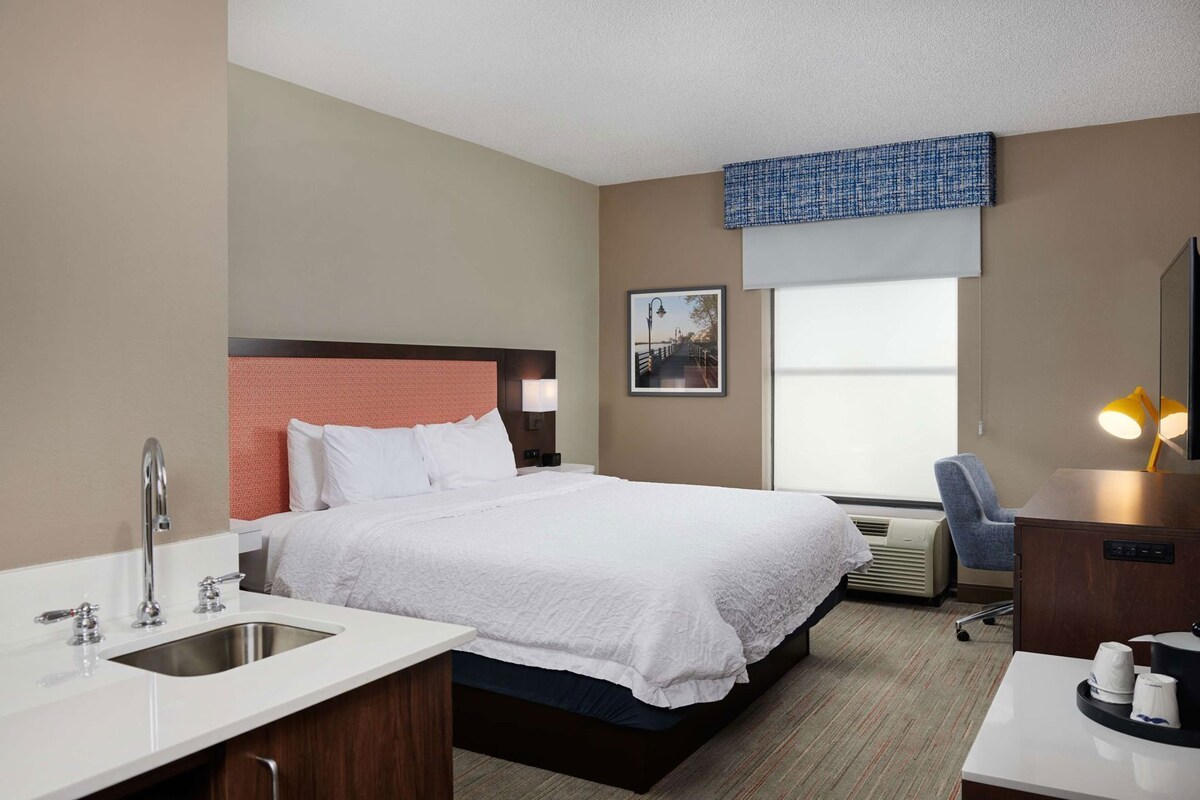 A hotel room with a bed, a desk, a chair, a sink, and a window with a view.